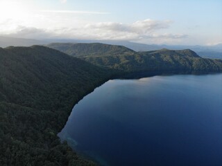 Obraz premium Drone aerial of deep blue mountain lake with forested shoreline and calm reflections at sunrise