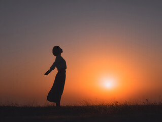 Silhouette of person standing in field at sunrise with arms outstretched, expressing freedom and peace in tranquil natural landscape