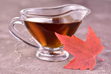 Maple syrup in a glass sauceboat on a gray background. Close-up.
