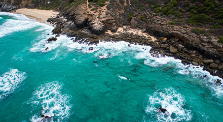 Stunning aerial view of turquoise ocean waves crashing on rocky coastline and sandy beach