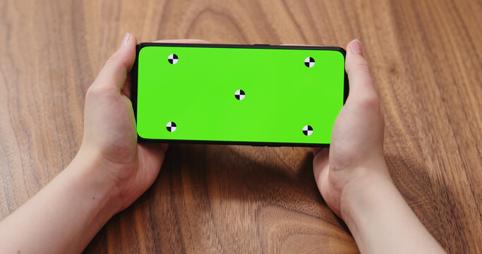 Young woman sitting at the table and using smartphone with green screen