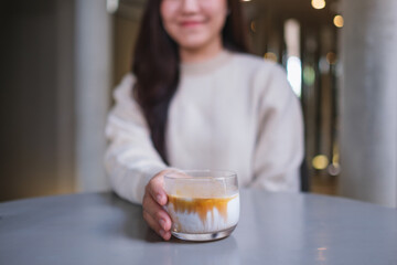 Closeup image of a woman holding and serving a glass of dirty coffee