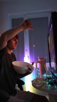Vertical screen frustrated young man throws popcorn and chips at screen showing anger disappointment and emotional outburst during online entertainment moment of modern digital frustration