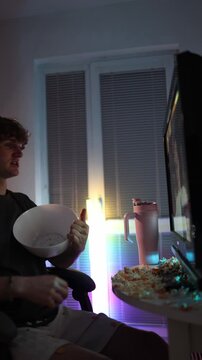 Vertical screen young man angrily throws popcorn at screen expressing frustration with content showing emotional reaction impulsive behavior and messy atmosphere of modern student life