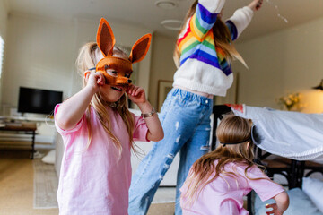Young girl holding her animal mask while her sisters are busy with their indoor cubbyhouse