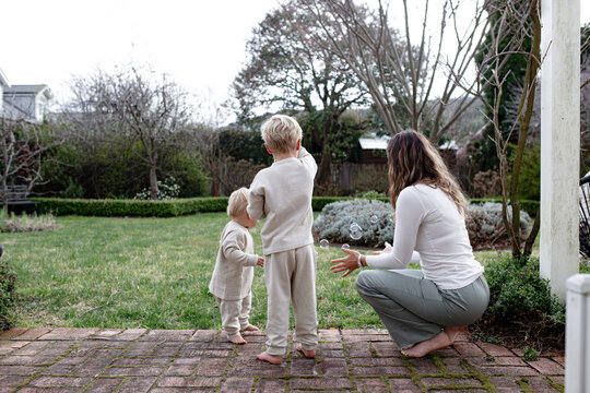 Young boys playing with bubble maker stick with mum in the garden