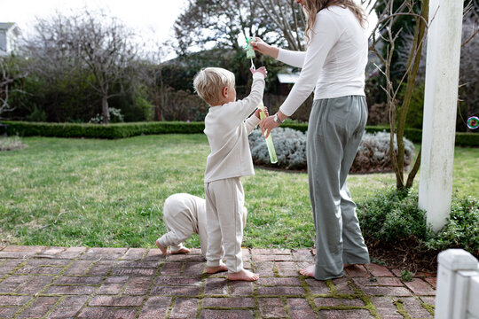 Young boys playing with bubble maker stick with mum in the garden