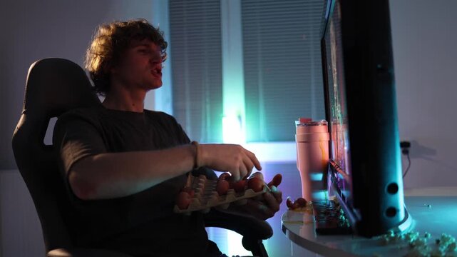 Young man throws eggs at the monitor at night frustrated by the content neon light spreads across the room creating chaotic messy scene full of impulsive emotion and sudden outburst