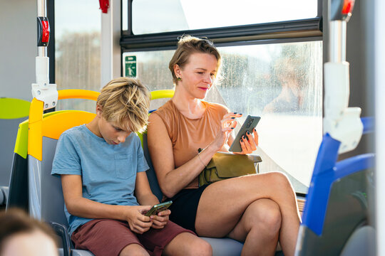 Mother and son traveling on a public bus, each engrossed in their smartphone, highlighting modern technology and screen time