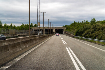 Highway leading to Peberholm tunnel of the Oresund Link between Denmark and Sweden under an overcast sky, concrete roadway and guardrails.