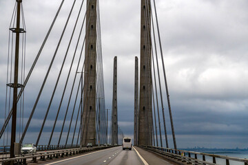 Vehicles driving along the Oresund bridge, a prominent cable stayed structure connecting Denmark and Sweden under a cloudy sky. 