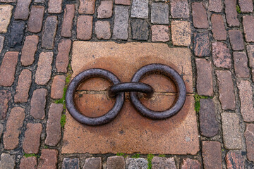 Linked metal rings on old cobblestone pavement in Denmark. Two linked antique iron mooring rings set in granite, surrounded by wet, weathered cobblestones rustic maritime urban detail.