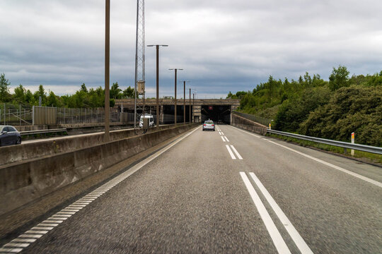Highway leading to Peberholm tunnel of the Oresund Link between Denmark and Sweden under an overcast sky, concrete roadway and guardrails. - Powered by Adobe