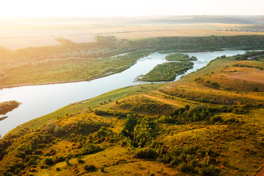 Top view over a tranquil river as golden sunlight dances on lush greenery in atmospheric landscape. Dniester canyon of Ukraine, Europe.
