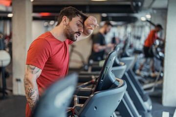 Young Tattooed Man And Senior Partner Exercising On Elliptical Machines In Contemporary Gym Setting