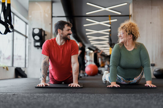 Young Adult Man And Woman Exercising Together Indoors In Bright Gym Wearing Casual Activewear - Powered by Adobe