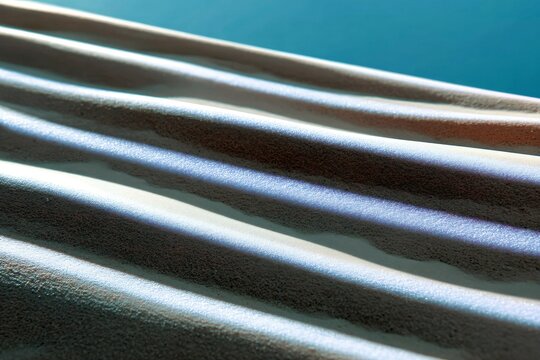A close-up abstract view of a textured surface with parallel ridges and valleys, illuminated by light and shadow.