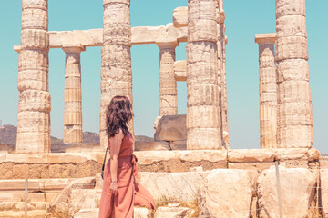 A young girl in a brown summer dress looking at the ancient temple of Poseidon on the Cape Sounion, closeup