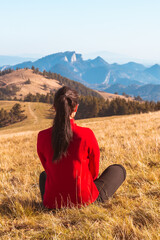 A young girl sits on the ground and looks at the beautiful panorama of autumn mountains