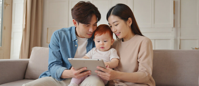 Modern Family Moment: A loving couple shares a special moment with their baby, engaging with a tablet in a cozy home setting, highlighting the bond of family and the simplicity of modern living.