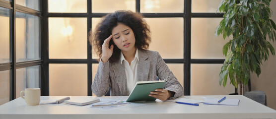 Concentration at Desk: An focused businesswoman immersed in her task at her desk, engrossed in a detailed examination of digital tablets.