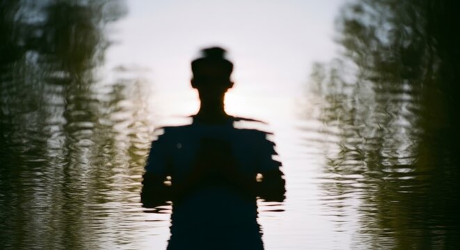 Mysterious silhouette of a person standing in serene rippling water at twilight reflection - Powered by Adobe
