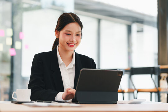 Happy smiling asian businesswoman professional working on tablet in modern office. Cheerful young female employee using technology for online job