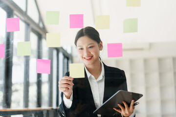 Confident asian businesswoman smiling while planning project strategy. Brainstorming new business idea with colorful note for task in office