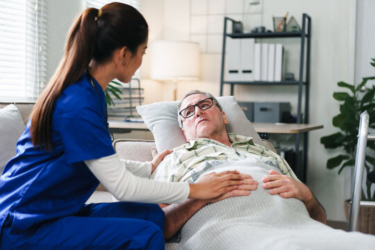 Young caregiver nurse elderly man bedside comforting patient with gentle touch and concerned expression