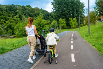 Mother pushing stroller and child riding bicycle in park enjoying family time