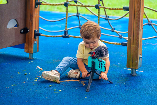 Kid playing with smartphone and microphone on tripod at playground
