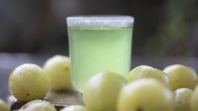 Close up of extracted beneficial juice of amla or Indian gooseberry or Phyllanthus emblica in a transparent glass on wooden surface with raw amla in a fruit basket.