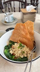 A bowl of noodle served with shredded chicken, vegetables and crackers