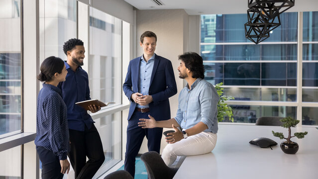 Smiling multiethnic professionals gather in boardroom engaged in informal conversation