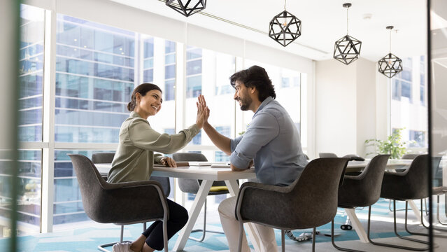 Smiling satisfied millennial businesswoman mature businessman partners exchange high fives