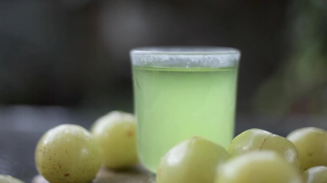 Close up of extracted beneficial juice of amla or Indian gooseberry or Phyllanthus emblica in a transparent glass on wooden surface with raw amla in a fruit basket.