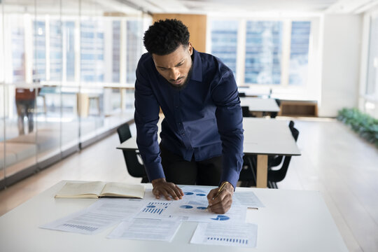 Young Black businessman stand at desk engaged in project research