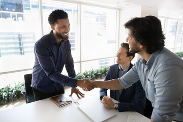 Friendly mature team leader shaking hand welcoming young male newcomer