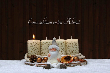 Erster Advent: Grußkarte zum ersten Advent, eine brennende Kerze mit  Weihnachtsschmuck im Schnee und dem Text einen schönen ersten Advent.