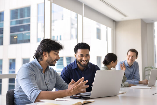 Indian man mentor Black male intern working together on notebook