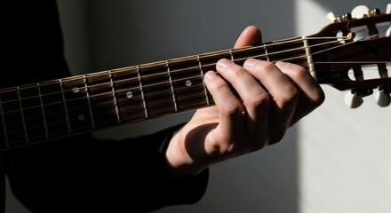 Close-up of a person's hand playing a guitar with a shallow depth of field in a dimly lit room with a moody atmosphere.