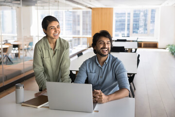 Laughing diverse teammates developing project in modern coworking at notebook
