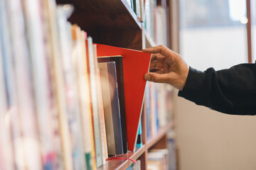 Hand picking a book from library shelf in warm sunlight, symbolizing education, knowledge, learning, research, and academic environment. Perfect for educational, library reading-related content.