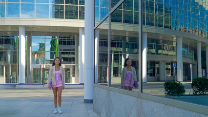 Young woman smiling standing confidently in front of a modern glass office building, showing her reflection
