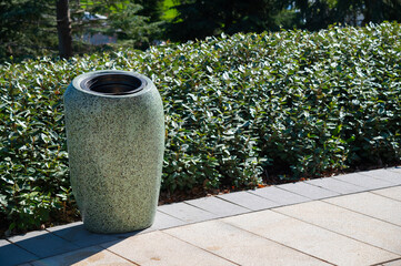 A streamlined trash can on a pedestrian path in a city park. Concrete street trash can	