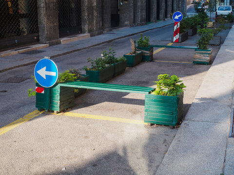 Wooden green benches bordering street planters, guiding pedestrian flow with traffic signs in historic Cremona, Italy