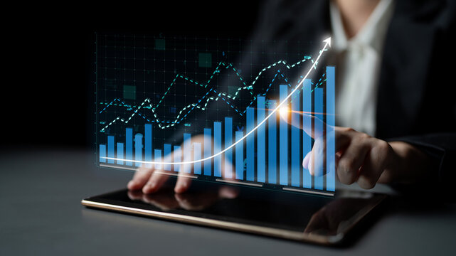 A business professional analyzes financial trends using a tablet, showcasing digital graphs and data in a dark environment, representing modern technology in finance. Impute