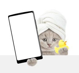 Funny tiny kitten with towel on it head holding rubber duck and  showing big smartphone with white blank screen in it paw above blank white banner. isolated on white background