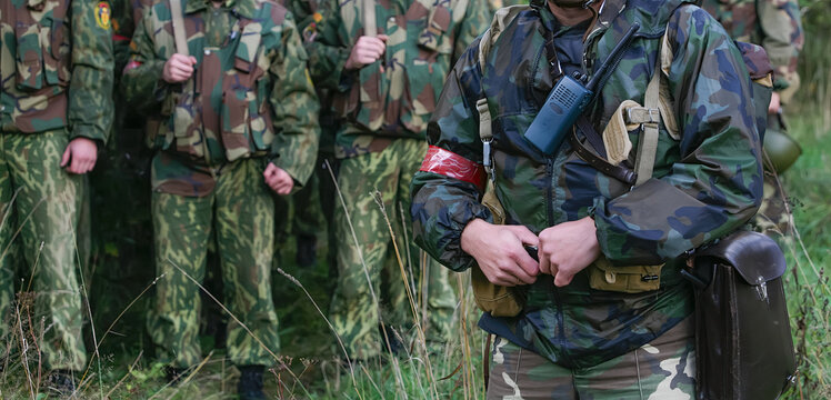 Soldiers in camouflage uniforms gather for a training exercise in a forest during early morning hours