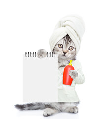Cute kitten with towel on it head wearing bathrobe standing on hind legs and holding bottle of shampoo and blank notepad. Empty space for text. Isolated on white background